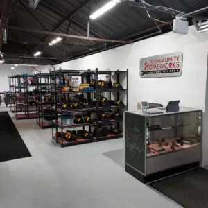 The interior of the Community Homeworks Kalamazoo tool library with rows of metal shelving units stocked with tools and a service counter featuring a sign that reads “Community Homeworks Tool Library.”.