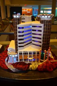 A large gingerbread model of a hotel with illuminated windows, resting on a base of red decorative fabric created for Community Homeworks Kalamazoo.