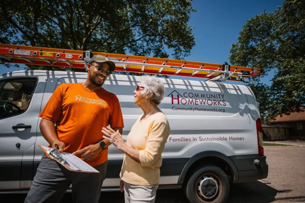 A Community Homeworks technician with a clipboard speaks to an older woman in front of a white work van in Kalamazoo.