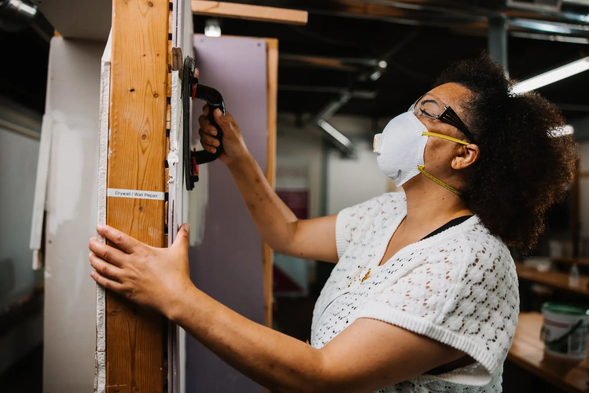 Woman wearing a face mask and safety goggles with a tool in hand.
