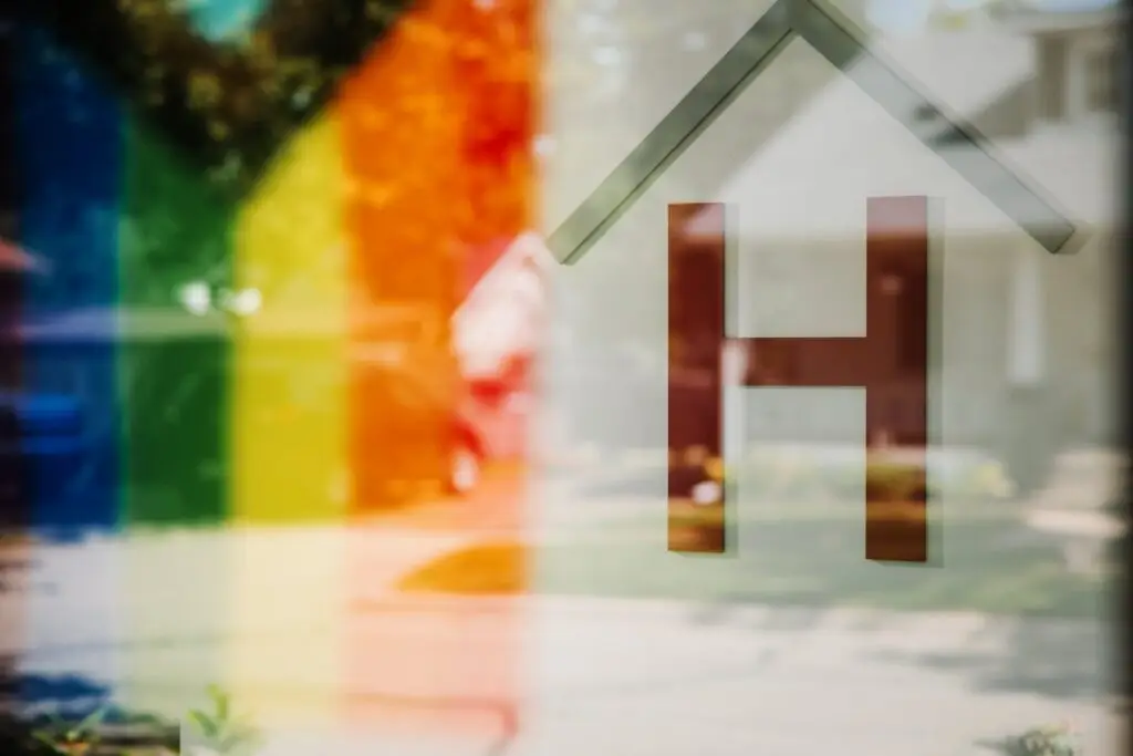 A glass surface displaying a rainbow stripe and the Community Homeworks Kalamazoo logo, which features a house with the letter H inside.
