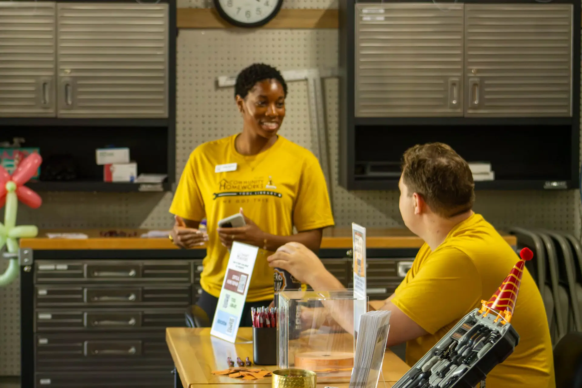 Two people in yellow Community Homework shirts talking to each other.